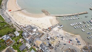 An aerial view of a coastal town with a sandy beach, a marina with numerous boats, and a mix of residential and commercial buildings. - Beachside paradise with hot tub and outdoor shower in Lyme Regis, Dorset (Lyme Regis)