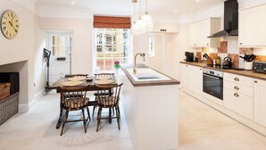 A modern kitchen with a dining area, featuring a large island, white cabinetry, and a built-in oven. - Beachside paradise with hot tub and outdoor shower in Lyme Regis, Dorset (Lyme Regis)