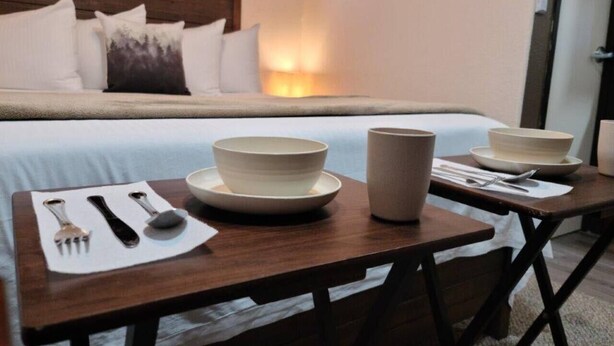A hotel room with a neatly made bed, a bedside table with a bowl, a cup, and cutlery. - 069A Private Studio nr South Rim Sleeps 4 (Williams)