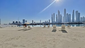 A beach with sun loungers and a city skyline in the background.