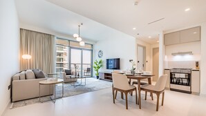 A modern living room with a sofa, coffee table, and dining area. There is a TV, a plant, and a kitchen area with an oven.