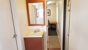 A narrow hallway leading to a bathroom with a sink, mirror, and wooden cabinet.