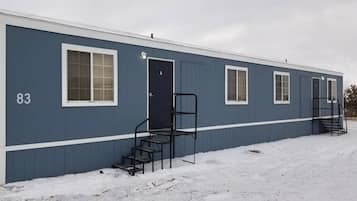 Een laag gebouw met een blauwe gevel, nummer 83, met een voordeur, twee ramen en een trap.