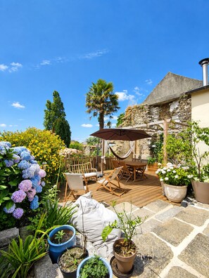 A patio area with a table and chairs, surrounded by potted plants and flowers. - Les Chambres D'Hespéris (Pleyben)