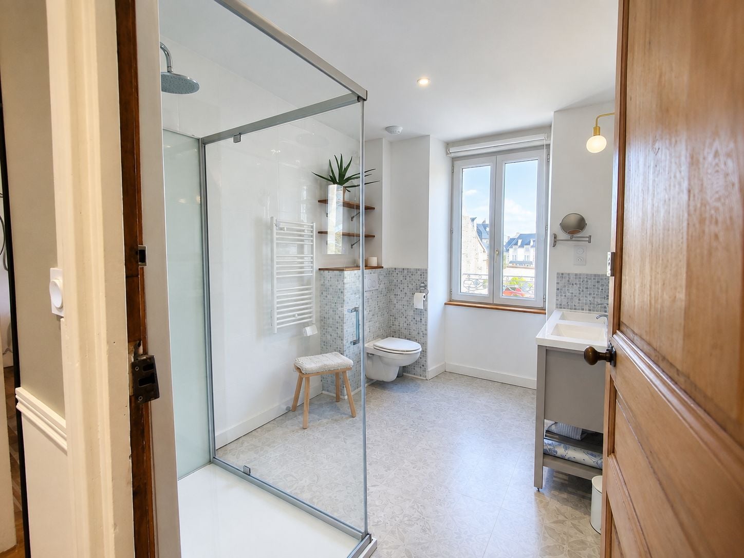 Ein modernes Badezimmer mit einer Duschkabine aus Glas, einer Toilette, einem Waschbecken und einem Fenster mit Blick nach außen.