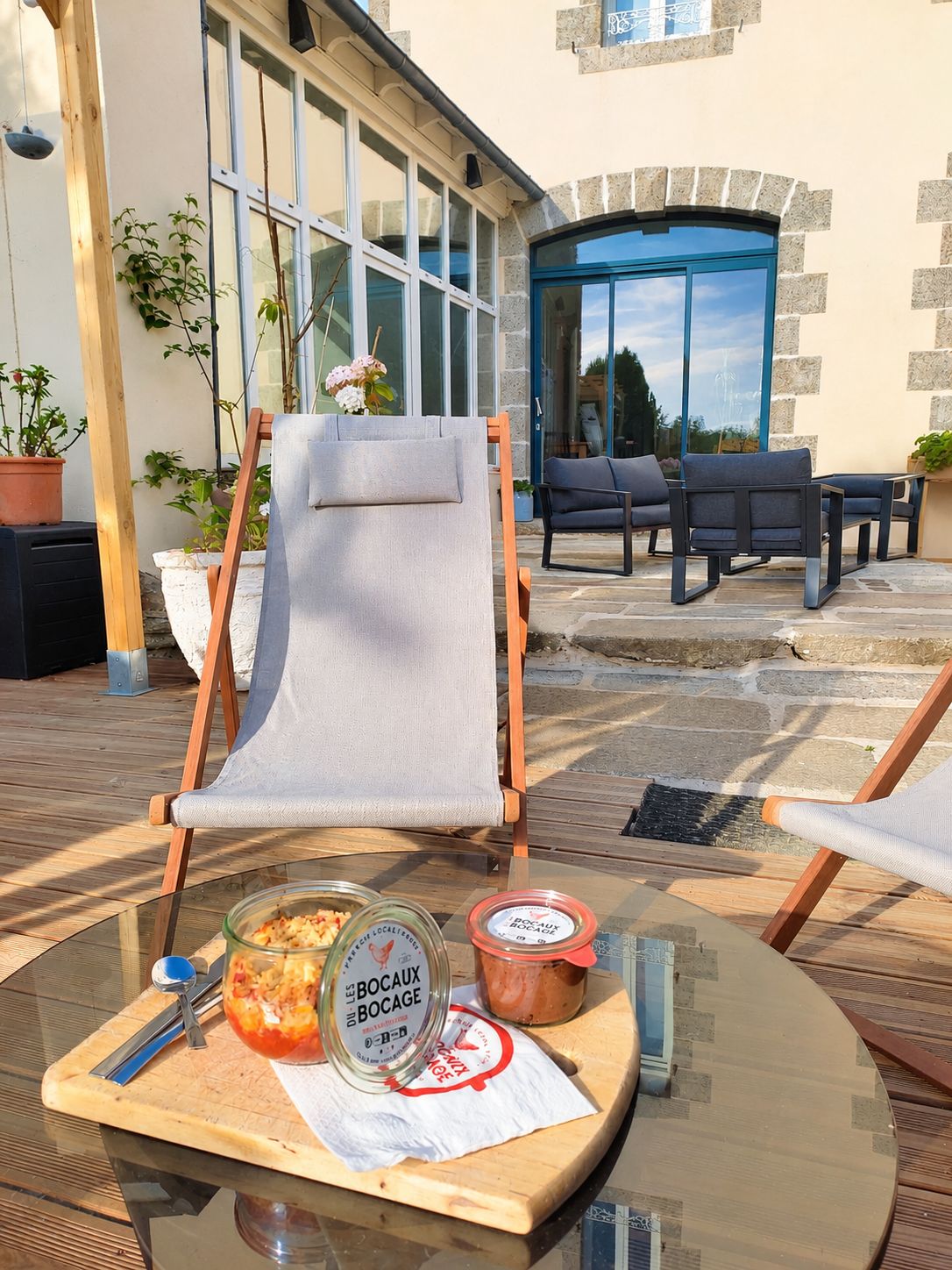 Un espace extérieur aménagé avec une table en verre, une chaise en toile et un présentoir en bois.