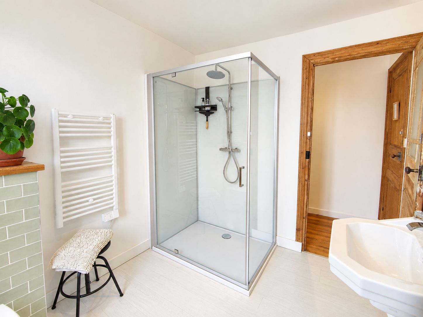 Een moderne badkamer met een douchecabine van glas, een witte wastafel en een houten deur.
