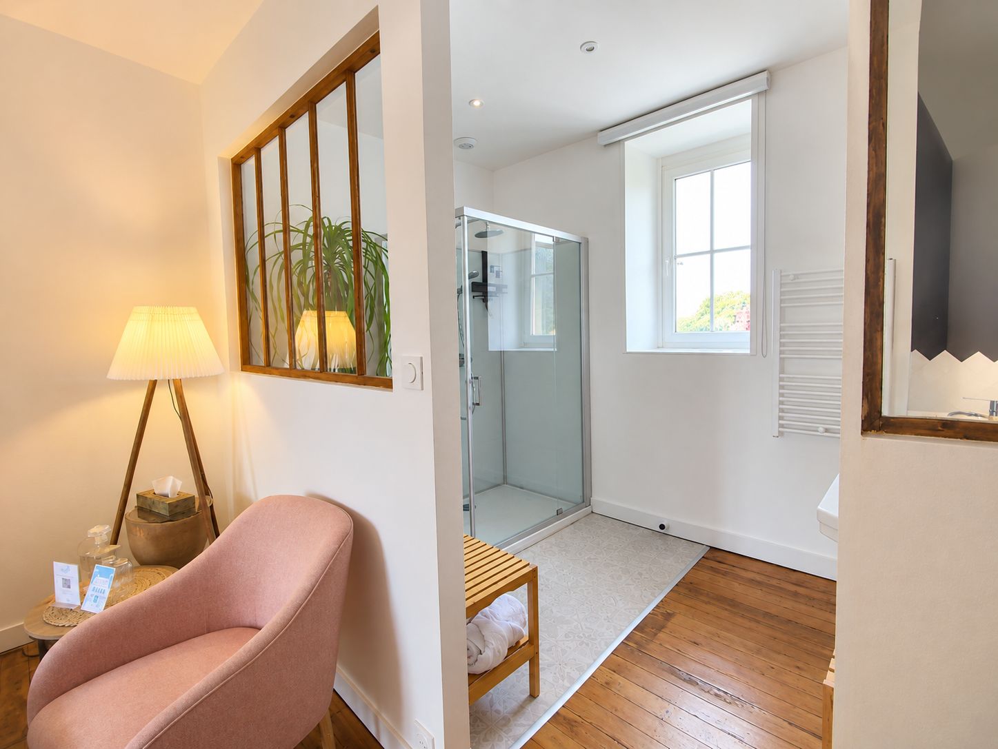 Een moderne badkamer met een douchecabine van glas, een houten vloer en een witte handdoek op een klein houten krukje.