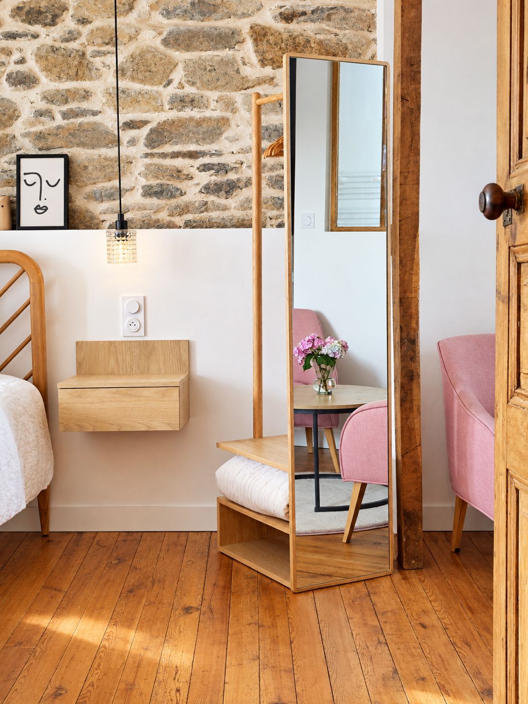 Une pièce avec un mur en pierre, une table de chevet en bois, un miroir, une chaise rose et une porte en bois.