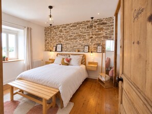 A bedroom with a stone wall, a wooden bed, bedside tables, a bench, and a wardrobe. - Les Chambres D'Hespéris (Pleyben)