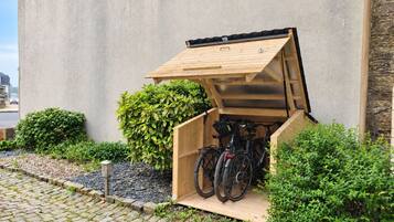 Een fietsenberging met een houten constructie tegen een gevel.