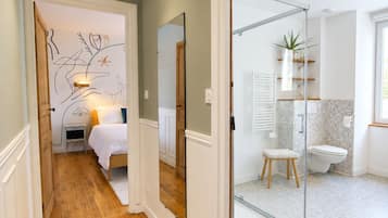 Een gang die uitkomt in een slaapkamer met houten vloer, een bed en een spiegel aan de muur.