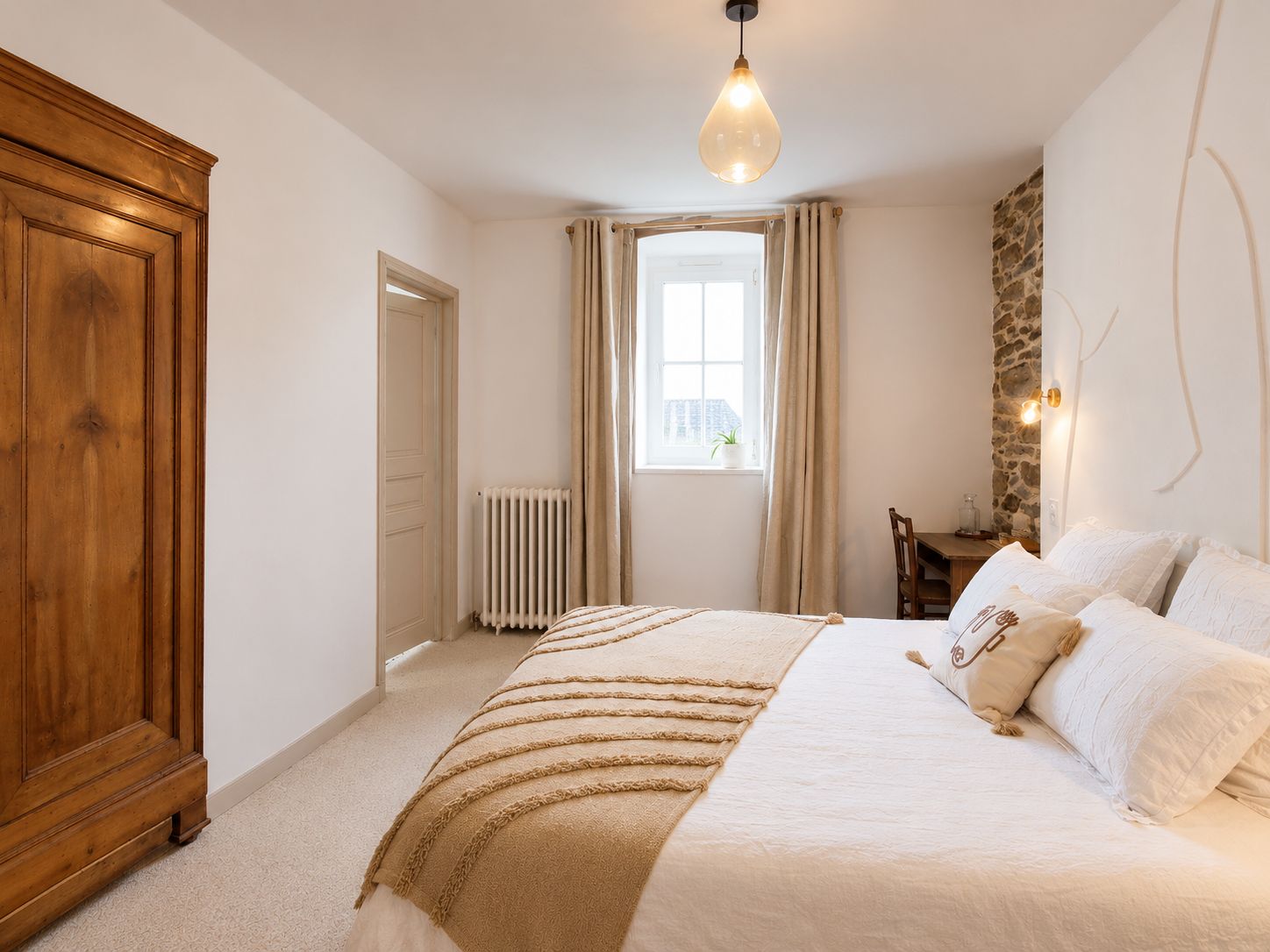 Een slaapkamer met een groot bed, een houten garderobe, een radiator, een raam met gordijnen en een stenen muur.