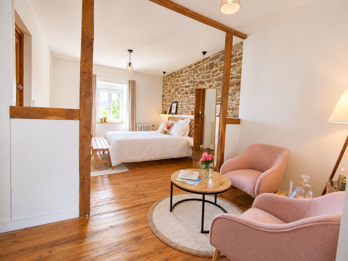 A bedroom with a bed, a sitting area with a chair and table, and a stone wall.