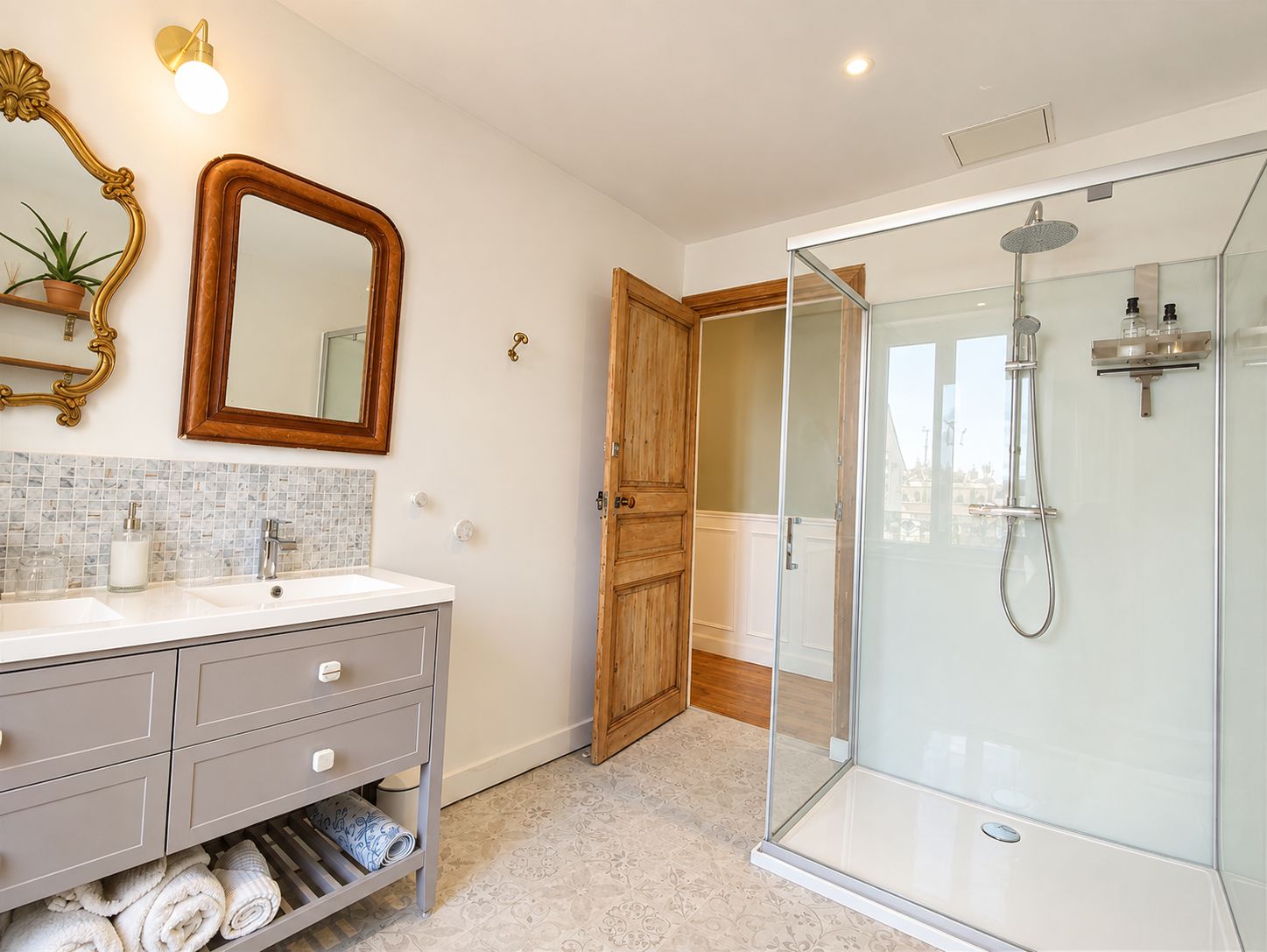 A bathroom with a glass-enclosed shower, a vanity with a mirror, and a door leading to another room.