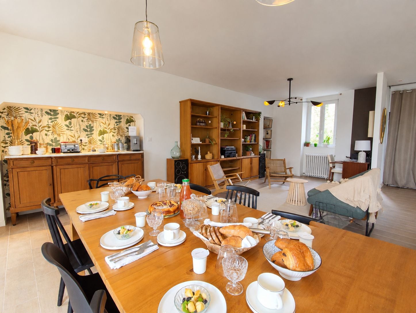 Un coin repas avec une table en bois mise pour le petit-déjeuner, entourée de chaises, avec une bibliothèque et un radiateur en arrière-plan.