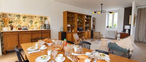 Un coin repas avec une table en bois mise pour le petit-déjeuner, entourée de chaises, avec une bibliothèque et un radiateur en arrière-plan.