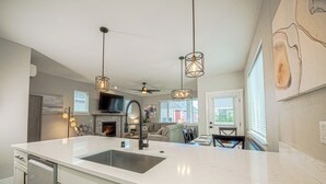 A modern kitchen with a large island, stainless steel appliances, pendant lighting, and a view to the living area.