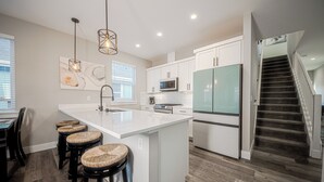 A modern kitchen with a large island, white cabinetry, and a stainless steel refrigerator.