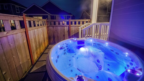 A hot tub with a wooden deck and a house in the background.