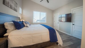 A bedroom with a bed, a ceiling fan, a window, and a TV.