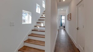 A modern interior with a wooden staircase, white walls, and a hallway leading to a bedroom.