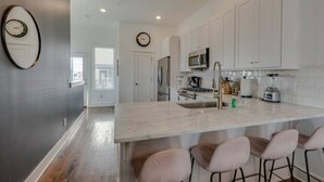 A modern kitchen with white cabinetry, a large island with bar stools, a microwave, stove, and a sink.