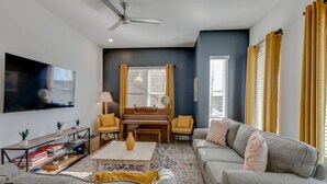 A living room with a piano, sofa, coffee table, and a flat-screen TV mounted on the wall.