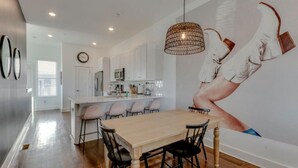 A modern kitchen with white cabinets, a dining area with a wooden table and black chairs, and a large abstract mural on the wall.