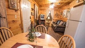 Un interior de cabaña acogedor con una mesa de comedor preparada para dos personas, un sofá, un televisor y un refrigerador.