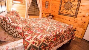 Un dormitorio acogedor de cabaña de madera con cama, cortinas, un cuadro enmarcado y una ventana con persianas.
