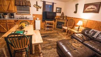 Una sala de estar acogedora con un sofá de cuero marrón, una mesa de comedor de madera con sillas, un televisor y una chimenea.