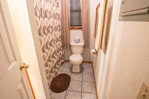 Un baño estrecho con inodoro, cortina de ducha estampada y una alfombra pequeña en el suelo.
