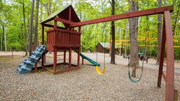 Un parque infantil con un tobogán de madera y columpios en un área boscosa.