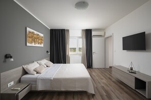 Een moderne hotelkamer met een bed, nachtkastje, televisie en uitzicht op het groen.