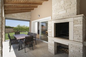 Une terrasse extérieure dotée d’une cheminée en pierre, d’une table à manger avec des chaises et offrant une vue sur le paysage environnant.