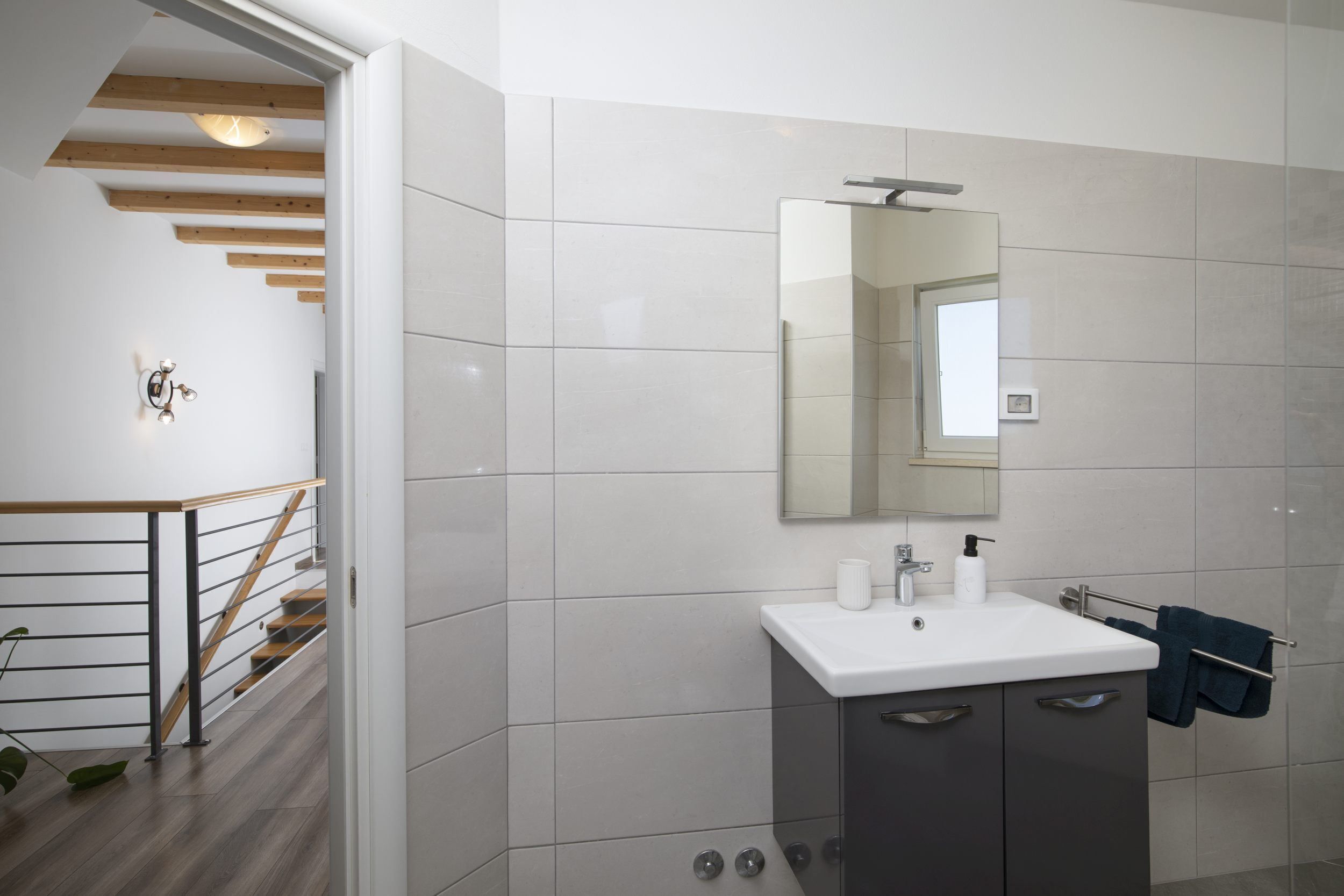 Un baño moderno con un lavabo blanco, un espejo y un perchero para toallas.