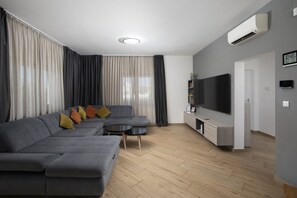 Un salon moderne avec un canapé d’angle gris, une petite table basse ronde et un téléviseur à écran plat fixé au mur.