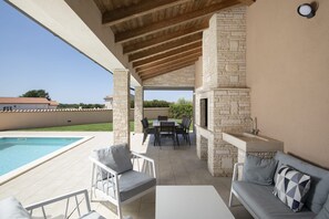 Une terrasse extérieure avec une piscine, des piliers en pierre, une table avec des chaises et un évier intégré.