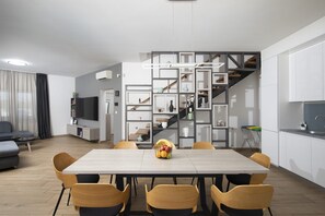 Eine moderne Küche mit weißen Schränken, einem Esstisch mit Stühlen und einer Treppe mit geometrischem Design.