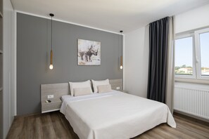 Une chambre à coucher avec un lit, des tables de chevet, une œuvre d’art accrochée au mur et une fenêtre avec des rideaux.