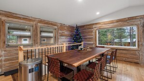 A wooden cabin interior with a dining table, chairs, a trash bin, and a Christmas tree. - Escape to our charming cabin, where rustic elegance meets modern comfort! (Wisconsin Dells)