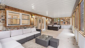 A covered outdoor living area with a stone wall, white cushioned seating, and a glass-top coffee table. - Escape to our charming cabin, where rustic elegance meets modern comfort! (Wisconsin Dells)