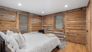 A log cabin bedroom with a bed, wooden walls, and a window with blinds. - Escape to our charming cabin, where rustic elegance meets modern comfort! (Wisconsin Dells)