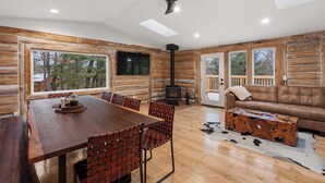 A log cabin interior with a dining area, a fireplace, a sofa, and large windows. - Escape to our charming cabin, where rustic elegance meets modern comfort! (Wisconsin Dells)
