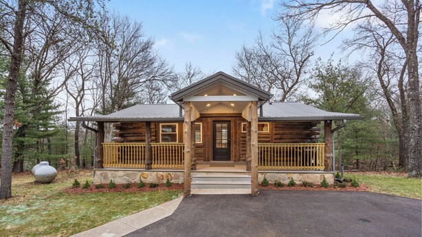 A log cabin with a porch, stone foundation, and a paved driveway. - Escape to our charming cabin, where rustic elegance meets modern comfort! (Wisconsin Dells)