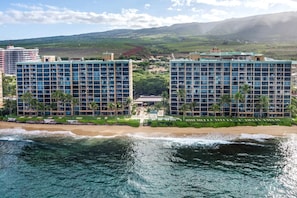 A beachfront hotel with multiple high-rise buildings, a swimming pool, and a view of the ocean and mountains.