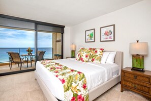 A bedroom with a bed, a nightstand, a chair, a table, and a view of the ocean.