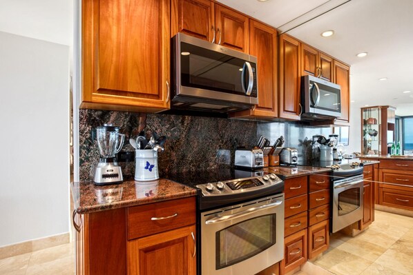 A modern kitchen with wooden cabinets, stainless steel appliances, granite countertops, and a view of the ocean.