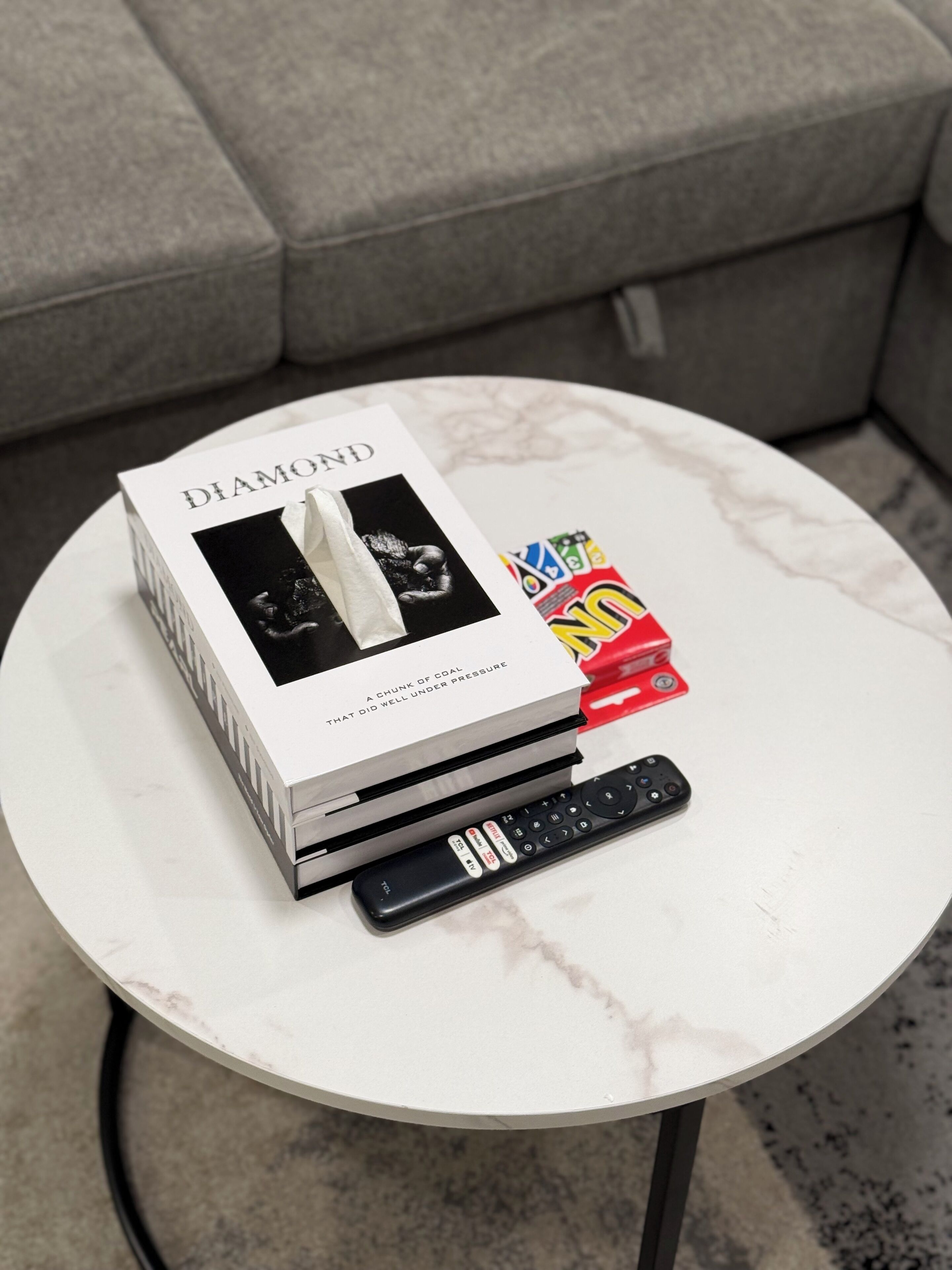 A white marble table with a book titled 'DIAMOND', a remote control, and a colorful box on it.